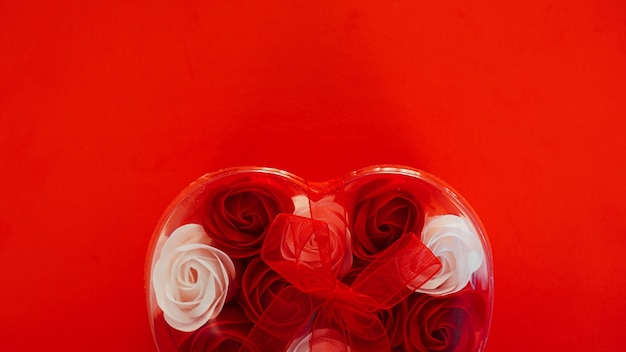 Walentynki prezent na czerwonym tle. dużo czerwonych i białych róż w opakowaniu w kształcie serca, przewiązanych czerwoną wstążką. pojęcie miłości