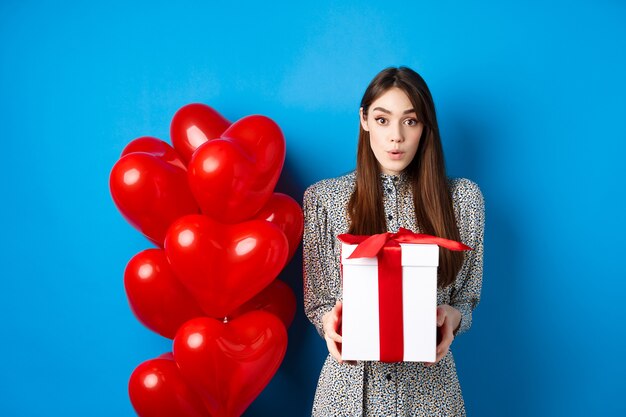 Walentynki zaskoczona atrakcyjna dziewczyna patrząca zdumiona w kamerę trzymająca wielki romantyczny prezent na stojąco...