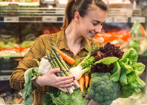 Warzywa organiczne z bliska. Piękna młoda kobieta robi zakupy w supermarkecie i kupuje świeżych organicznie warzywa