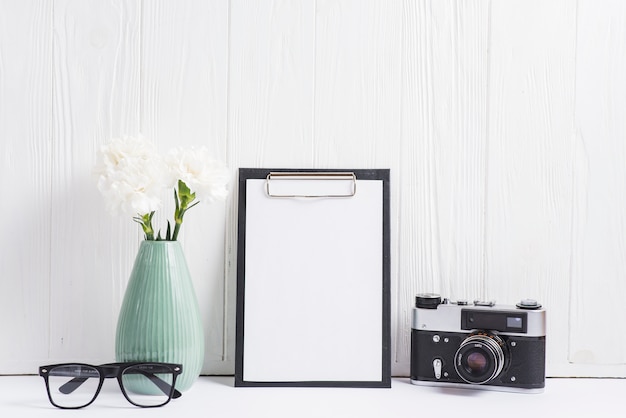 Bezpłatne zdjęcie wazon; okulary; aparat fotograficzny i czysty papier w schowku przed puste drewniane ściany