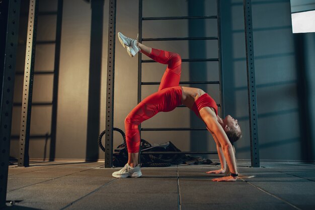 Wdzięczny. Młody mięśni kaukaski kobieta ćwiczy w siłowni. Lekkoatletyczna modelka robi ćwiczenia siłowe, trenuje jej dolną, górną część ciała, rozciąganie. Wellness, zdrowy tryb życia, kulturystyka.