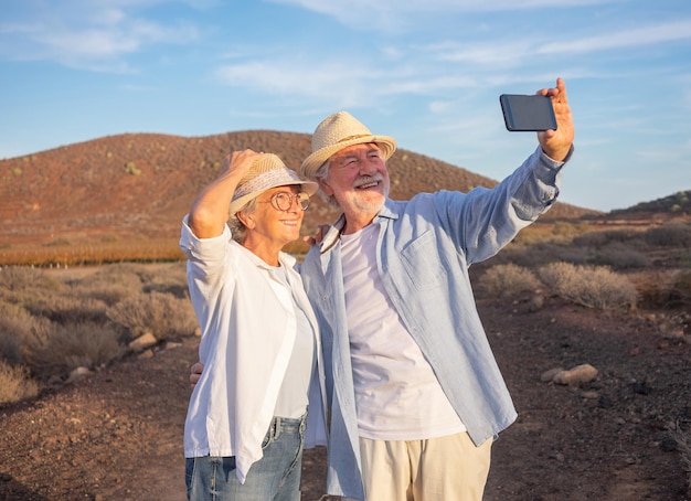 Wesoła, aktywna starsza para starszych, ciesząca się na zewnątrz przy świetle zachodu słońca, robiąca selfie z telefonem