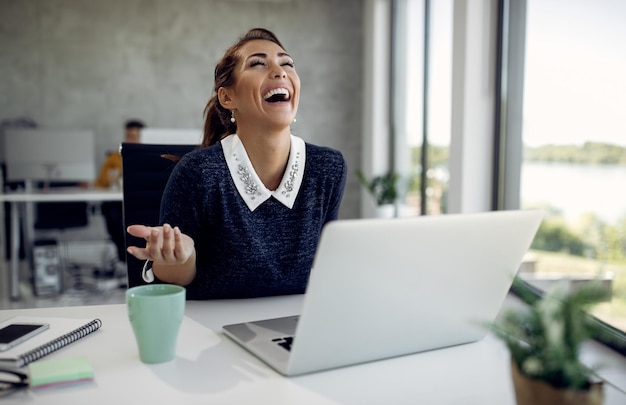 Bezpłatne zdjęcie wesoła bizneswoman bawi się podczas korzystania z laptopa w biurze