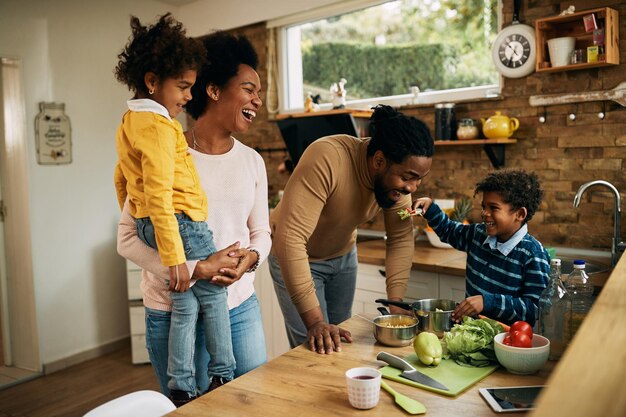 Wesoła czarna rodzina bawi się zdrowym jedzeniem w kuchni