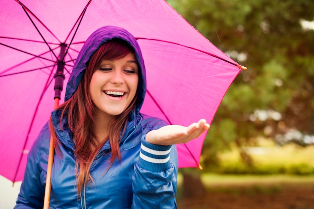 Wesoła kobieta pod różowym parasolem sprawdzanie deszczu