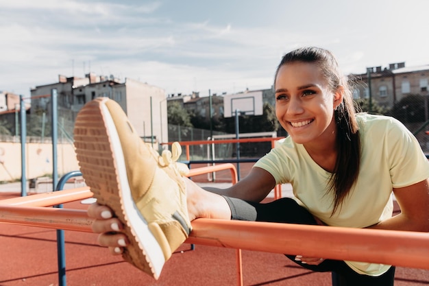 Wesoła kobieta rozciągająca nogi na boisku sportowym