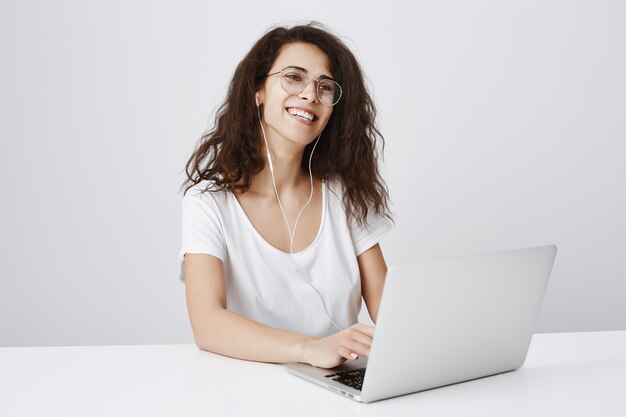 Wesoła kobieta śmiejąc się podczas pracy z laptopem i słuchania muzyki w słuchawkach
