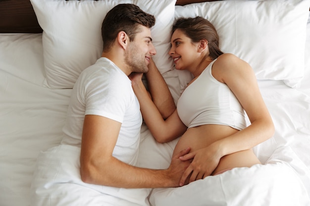 Wesoła kobieta w ciąży leży w łóżku z mężem