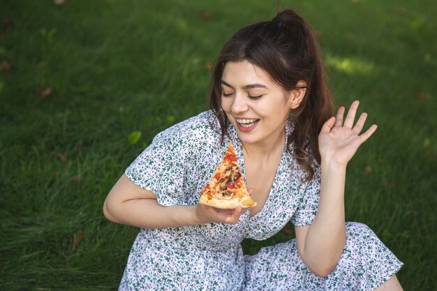 Wesoła młoda kobieta z kawałkiem pizzy na pikniku