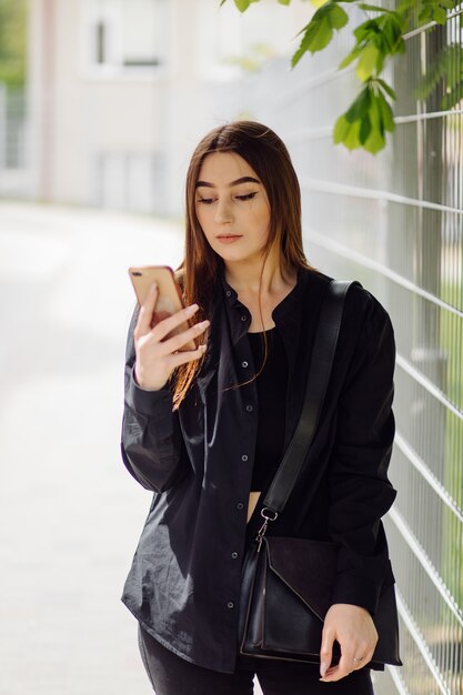 Wesoła piękna brunetka kobieta w dobrym nastroju używa telefonu na zewnątrz