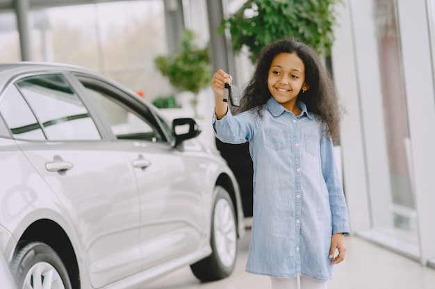 Wesoła, śliczna mała dziewczynka trzyma kluczyki do samochodu, pokazuje to, uśmiecha się i pozuje.