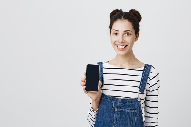 Wesoła, uśmiechnięta kobieta pokazuje aplikację na smartfonie na ekranie