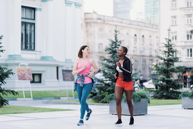 Wesoła uśmiechnięta koleżanka w sportowej stroju biegająca po mieście rozmawiająca o wieloetnicznych kobietach podczas treningu fitness