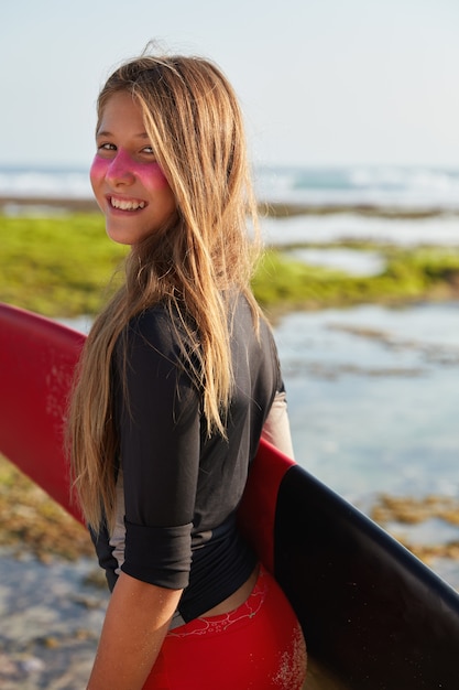 Bezpłatne zdjęcie wesoły aktywny surfingowiec o sportowej sylwetce, przygotowuje się do lokalnych zawodów surfingowych