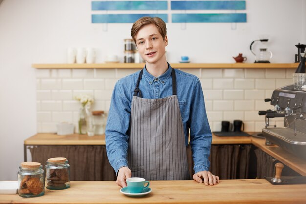 Wesoły barista w barze licznika. Daje klientowi zamówioną kawę.