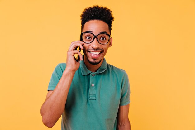 Wesoły facet rozmawia przez telefon w modnej zielonej koszulce. Beztroski młody człowiek trzyma smartphone i uśmiecha się.