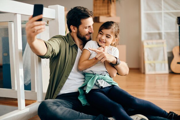 Wesoły ojciec i córka odbywają rozmowę wideo przez smartfona w swoim nowym domu