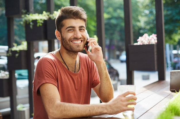 Wesoły przystojny mężczyzna, śmiejąc się i uśmiechając, rozmawiając przez telefon komórkowy z kawiarni na świeżym powietrzu