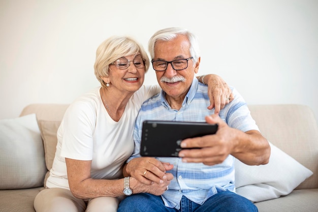 Wesoły seniorzy surfują po Internecie z tabletemrodzinna technologia wiekowa i koncepcja ludzi szczęśliwa para starszych z komputerem typu tablet w domu