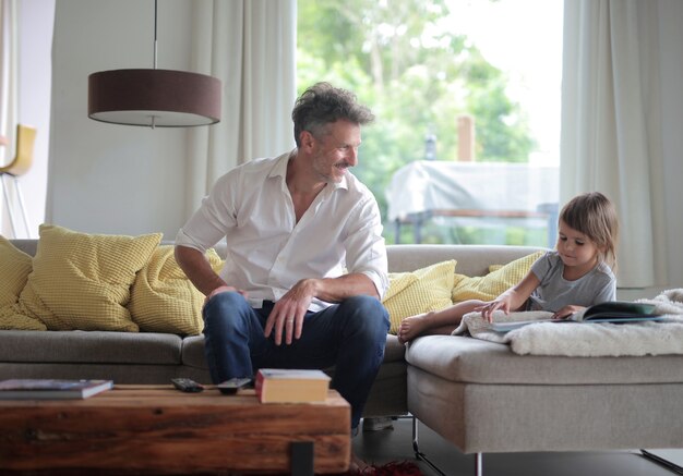 Wesoły tata i jego dziecko oglądają zdjęcia w albumie fotograficznym na kanapie