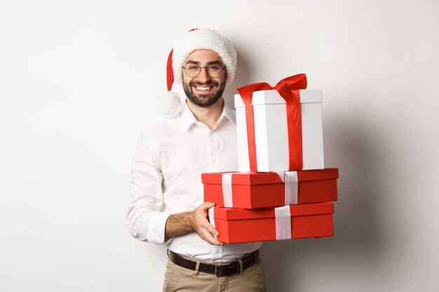 Wesołych Świąt Bożego Narodzenia, koncepcja wakacji. Szczęśliwy młody człowiek uśmiechnięty, trzymając prezenty w pudełkach i nosząc kapelusz santa