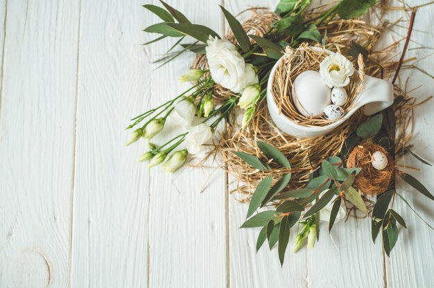 Wesołych Świąt Wielkanocnych. Pisanki w filiżance na drewnianym białym tle z kwiatową dekoracją. Koncepcja Wesołych Świąt