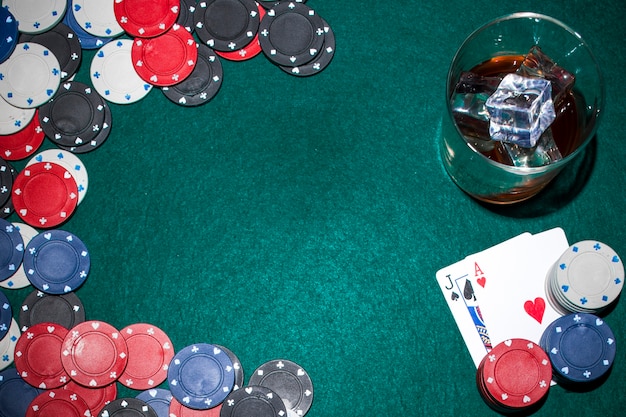 Whisky z kostkami lodu i żetony i karty do gry na zielonym stole pokerowym