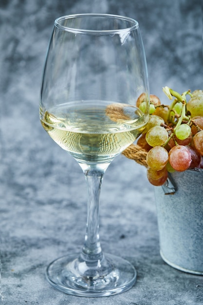 Wiaderko winogron i kieliszek wina na niebieskiej powierzchni.