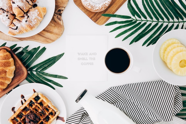 Wiadomość na notatniku otoczona pieczonym śniadaniem; kawa i plasterki ananasa na białym biurku