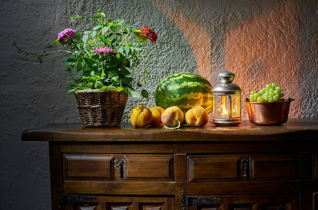 Widok arbuza, moreli, winogron, świeżych kwiatów i abażuru na drewnianym stole