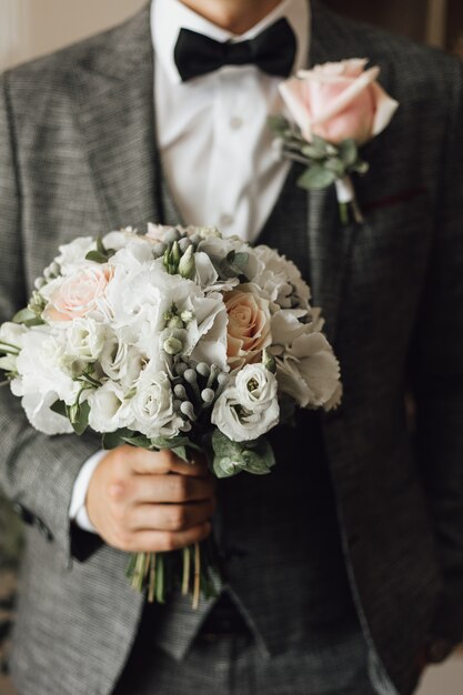 Widok klatki piersiowej mężczyzny ubranego w stylowy szary garnitur z bukietem ślubnym i boutonniere