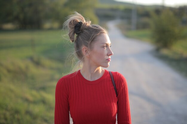 Widok kobiety ubranej w czerwoną bluzkę i cieszącej się słonecznym dniem na łonie natury przy drodze