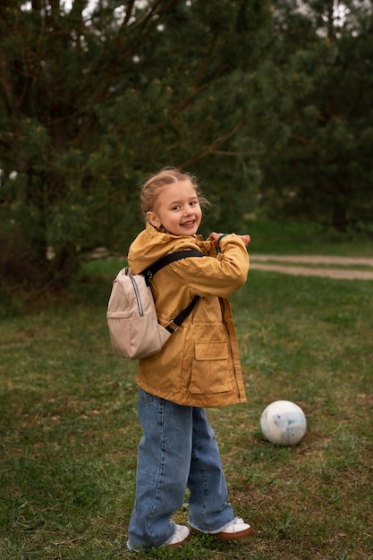 Bezpłatne zdjęcie widok małej dziewczynki z plecakiem podróżującej w przyrodzie i grającej w piłkę