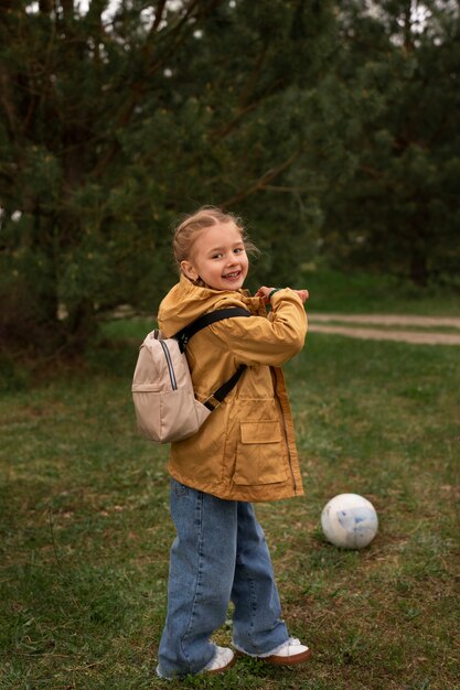 Widok małej dziewczynki z plecakiem podróżującej w przyrodzie i grającej w piłkę