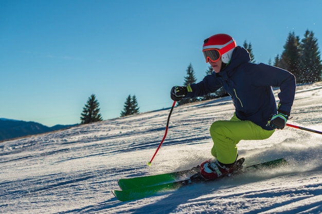 Widok mężczyzny na sobie zielone spodnie i jasny pomarańczowy kask podczas jazdy na nartach w słoneczny dzień