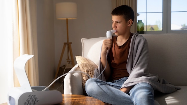 Bezpłatne zdjęcie widok nastoletniego chłopca używającego inhalatora w domu w przypadku problemów ze zdrowiem układu oddechowego