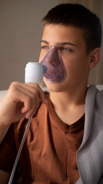 Widok nastoletniego chłopca używającego nebulizatora w domu w przypadku problemów ze zdrowiem układu oddechowego