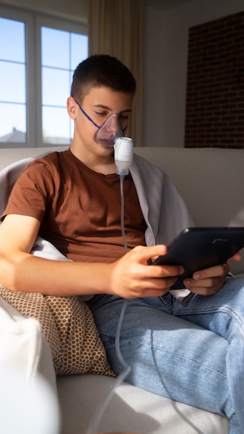 Bezpłatne zdjęcie widok nastoletniego chłopca używającego nebulizatora w domu w przypadku problemów ze zdrowiem układu oddechowego