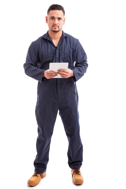 Bezpłatne zdjęcie widok pełnej długości przedstawiający młodego mężczyznę w kombinezonie i używającego komputera typu tablet do pracy