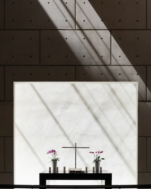 Widok pionowy wazonów i krzyża na stole w pokoju z betonową ścianą