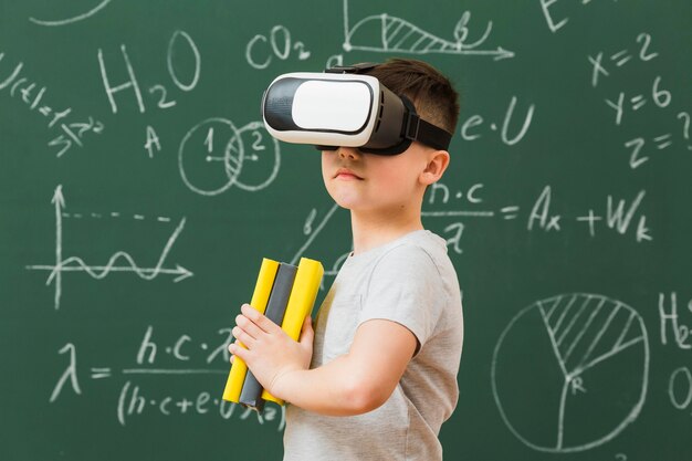 Widok z boku chłopca na sobie słuchawki wirtualnej rzeczywistości i trzyma książki