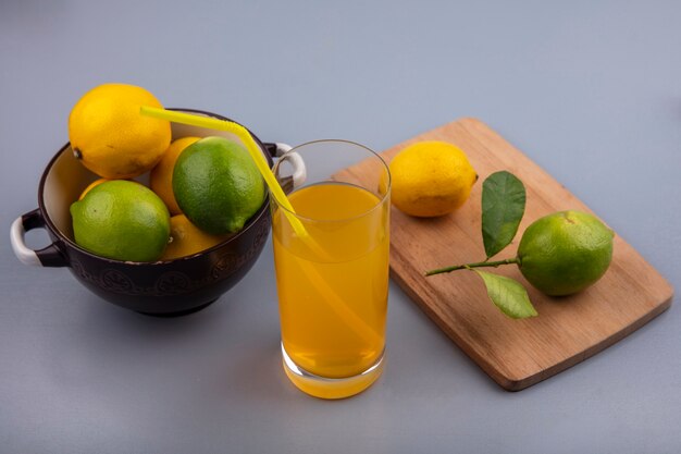 Widok z boku cytryny z limonki w rondlu z deską do krojenia i sokiem pomarańczowym na szarym tle