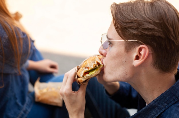 Widok z boku człowieka jedzenie burgera na zewnątrz