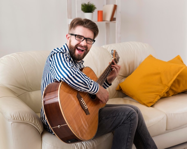 Bezpłatne zdjęcie widok z boku człowieka na kanapie, gra na gitarze