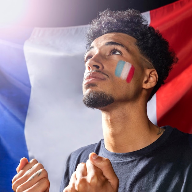 Widok z boku człowieka z flagą francuską, patrząc w górę i trzymając razem pięści