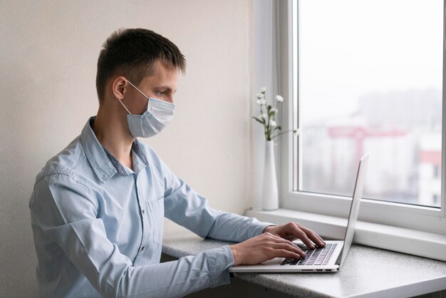 Widok z boku człowieka z maską medyczną pracującego na smartfonie