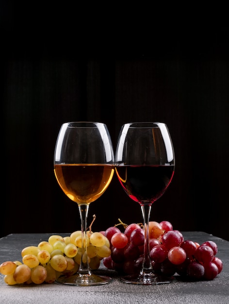 Widok z boku kieliszki do wina z winogron na czarnym pionie