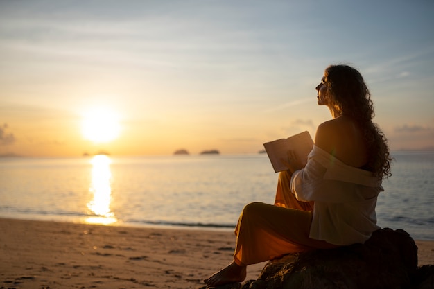 Bezpłatne zdjęcie widok z boku kobieta czytająca na plaży