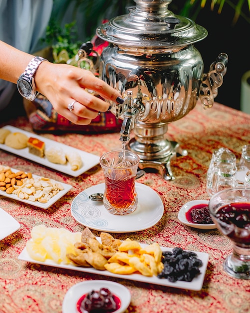 Widok z boku kobieta nalewa herbatę z czajnika samowar do szklanki armudy na spodku