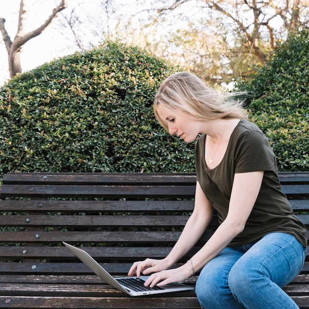 Widok z boku kobieta używa laptop na ławce